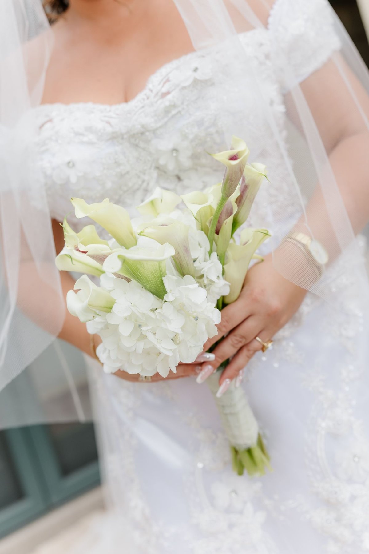 Abigail holding a white bridal bouquet against her lace wedding dress