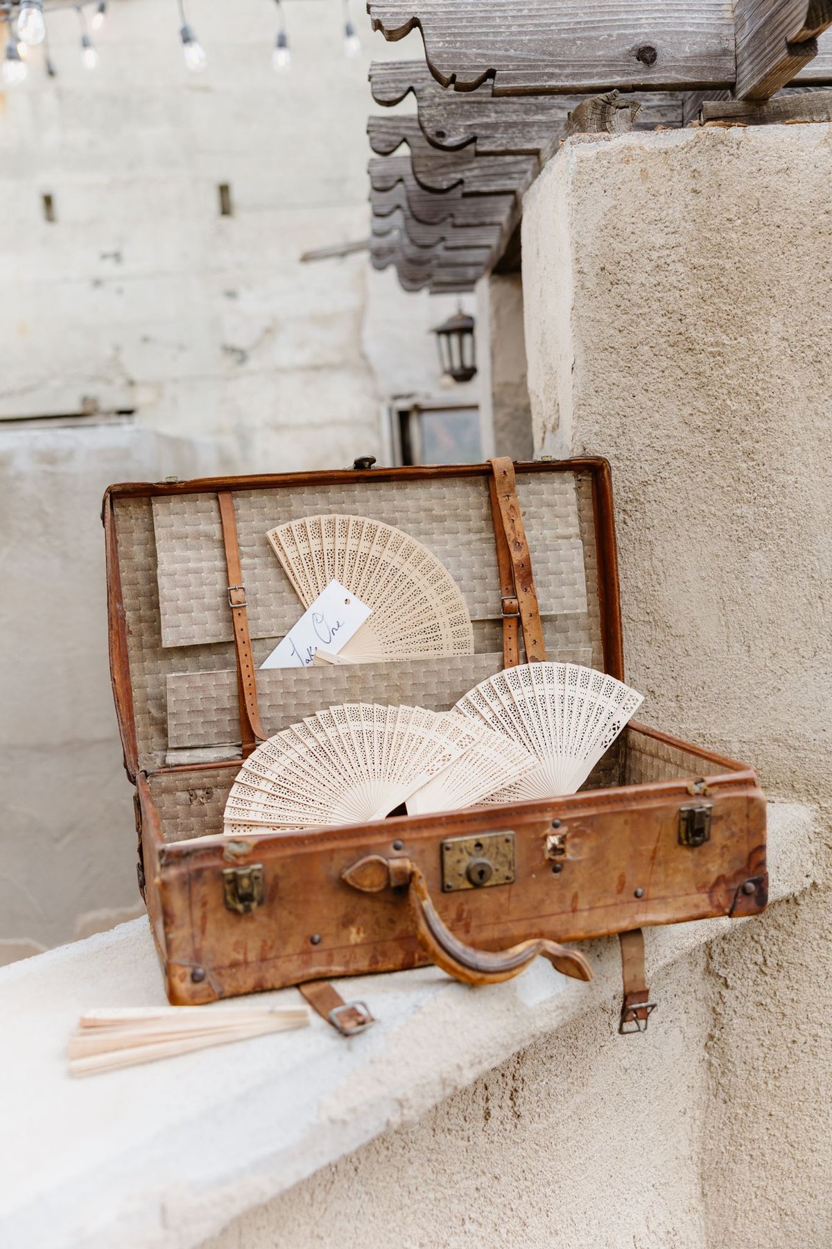 Hand fans displayed in a vintage suitcase for wedding guests