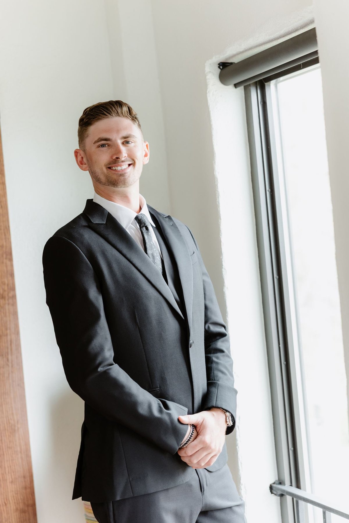 Ethan standing beside a window in his wedding suit