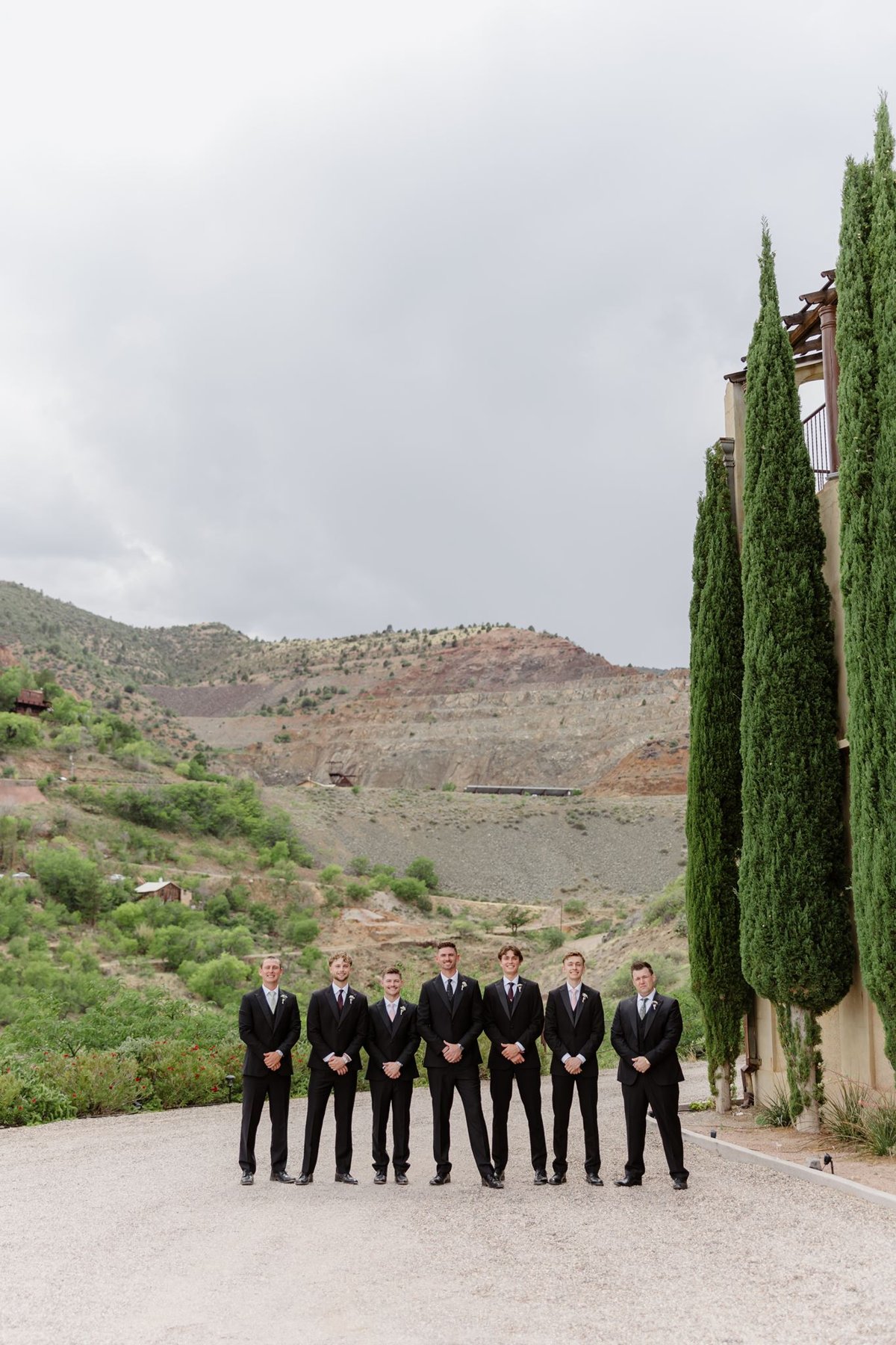 Groomsmen standing beside the estate’s tall cypress trees