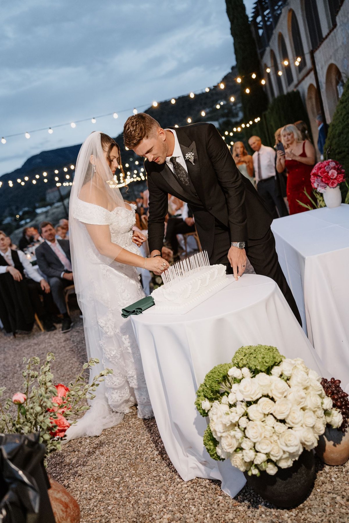 Abigail and Ethan cutting their wedding cake beneath string lights