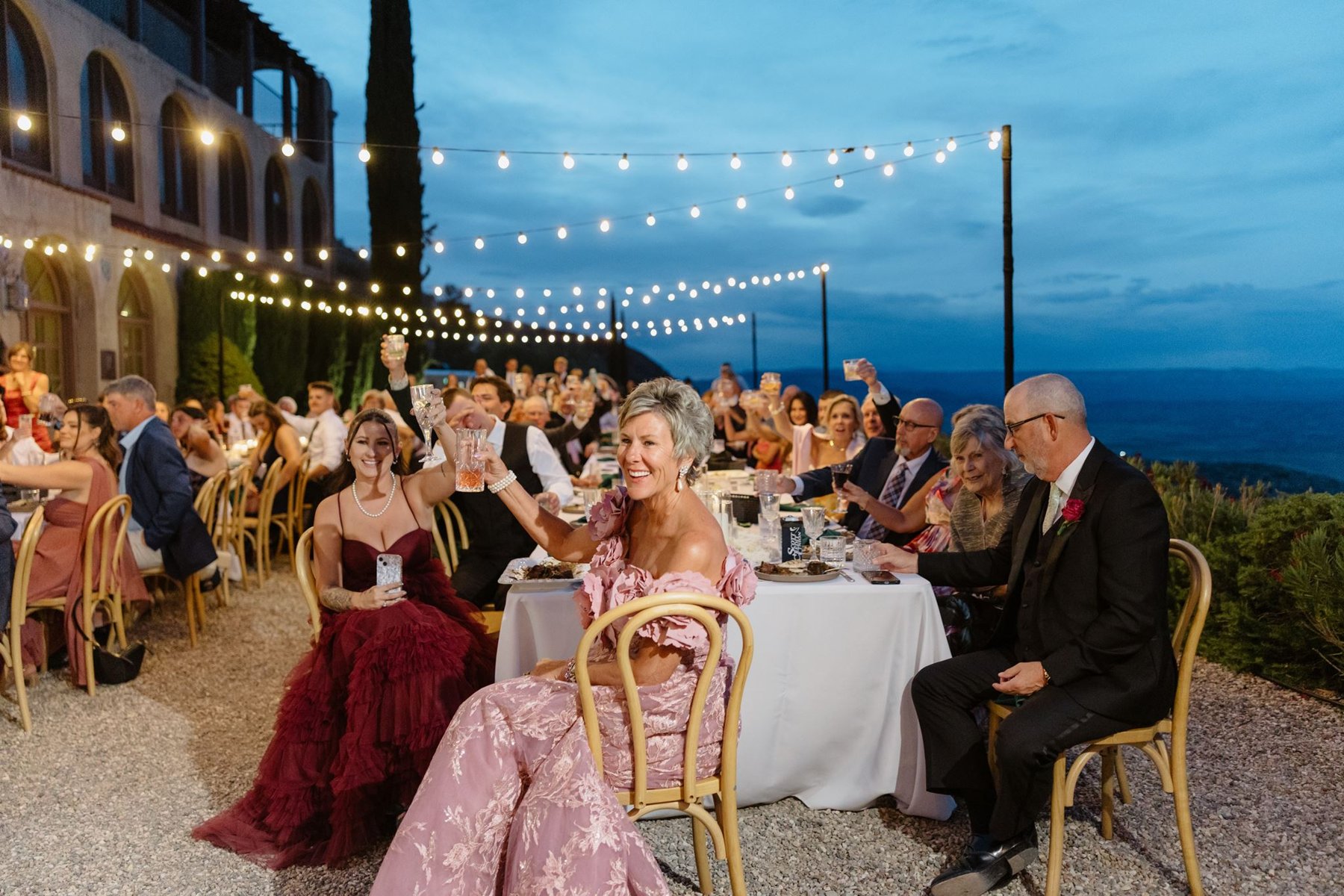Wedding guests raising their glasses beneath the reception string lights