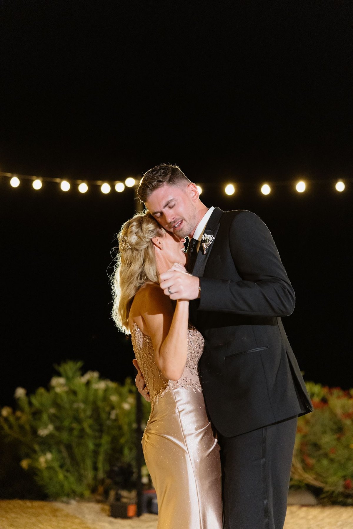 Ethan hugging his mother during their dance beneath string lights