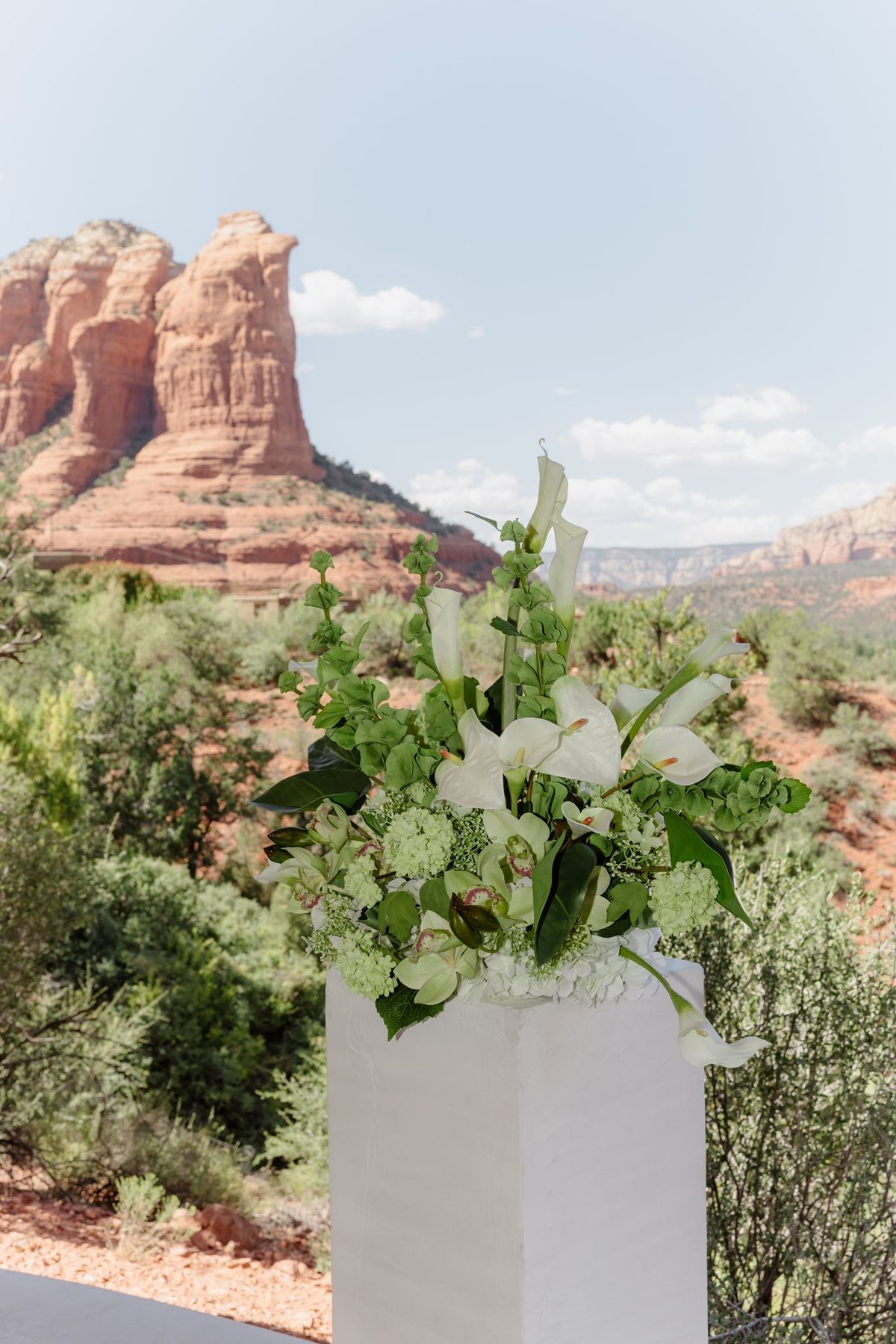White and green ceremony flowers on a pedestal with Sedona red rocks behind them at Eagle Dancer
