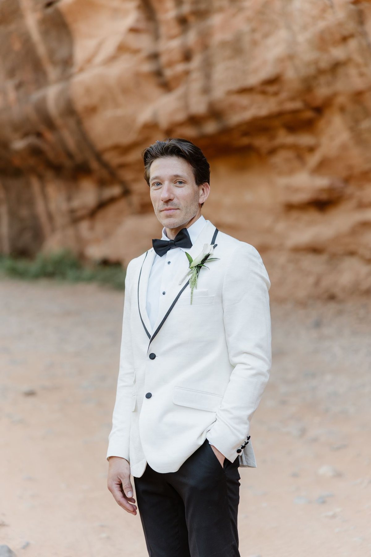 Brandon wearing his white jacket and boutonniere in front of Sedona sandstone