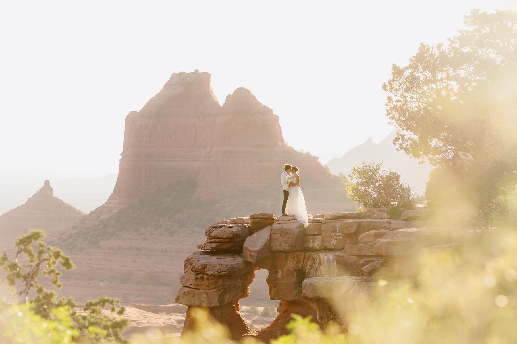 Maggie and Brandon on a rock overlook at Merry-Go-Round Rock with golden light and Sedona cliffs behind them