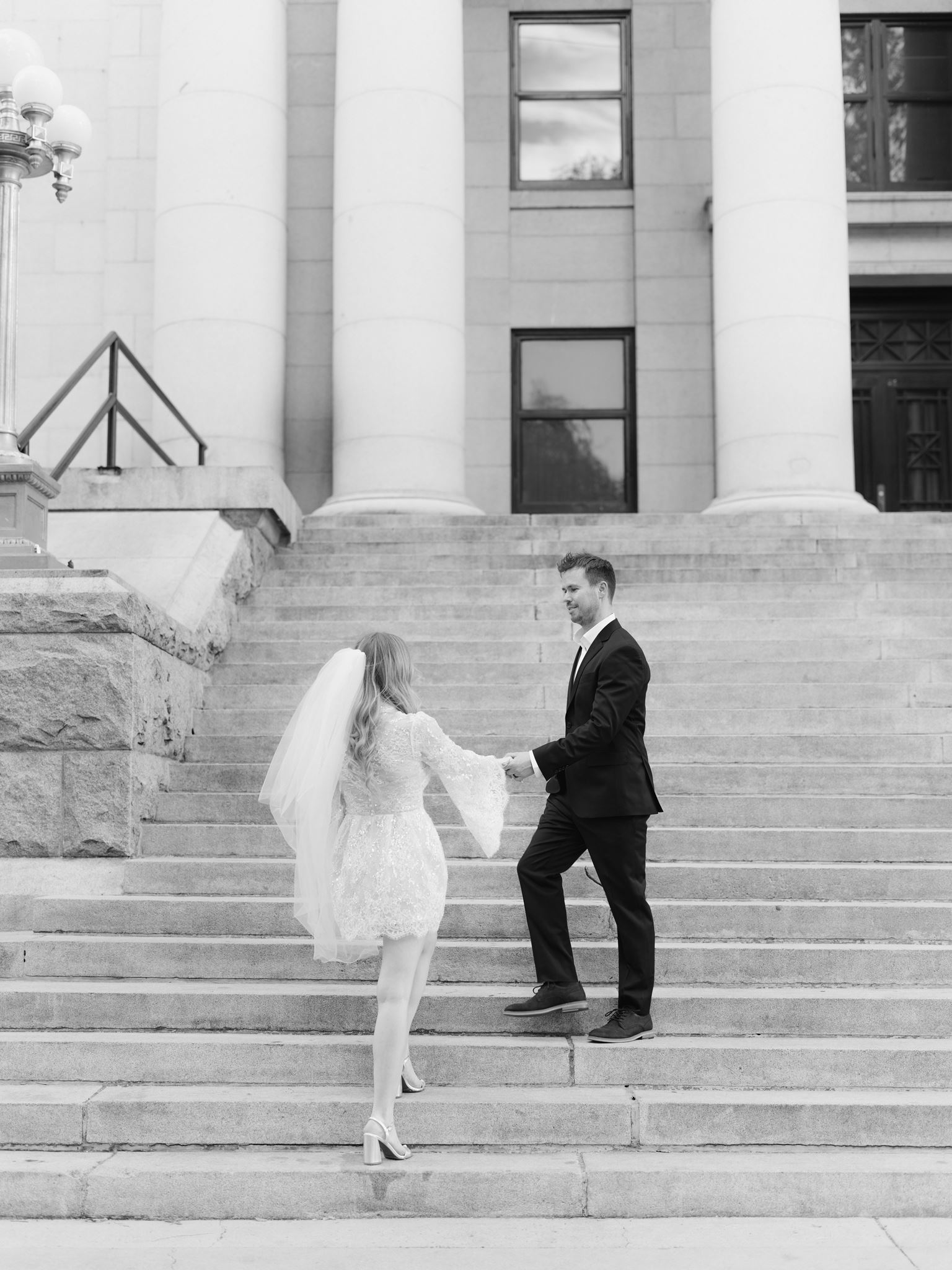 Black and white portrait of the couple holding hands on the courthouse stairs.