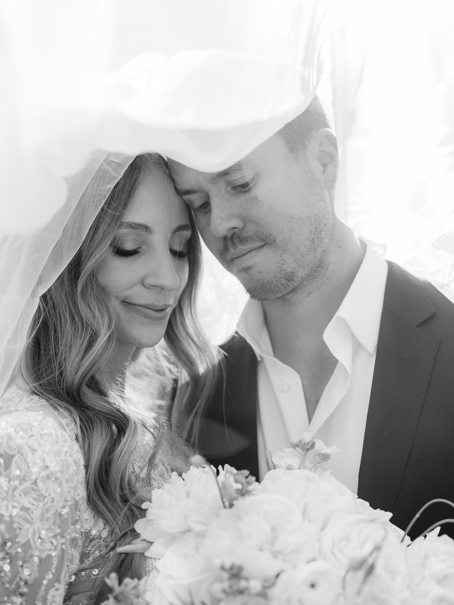 Black and white close portrait of Erica and Evan beneath the veil with white flowers.