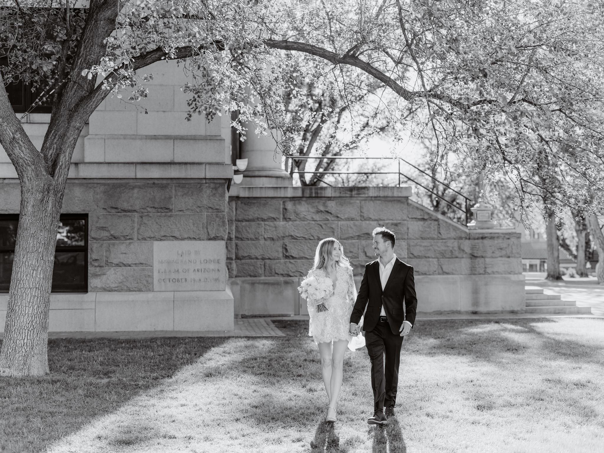 Black and white portrait of Erica and Evan walking hand in hand on the courthouse lawn.