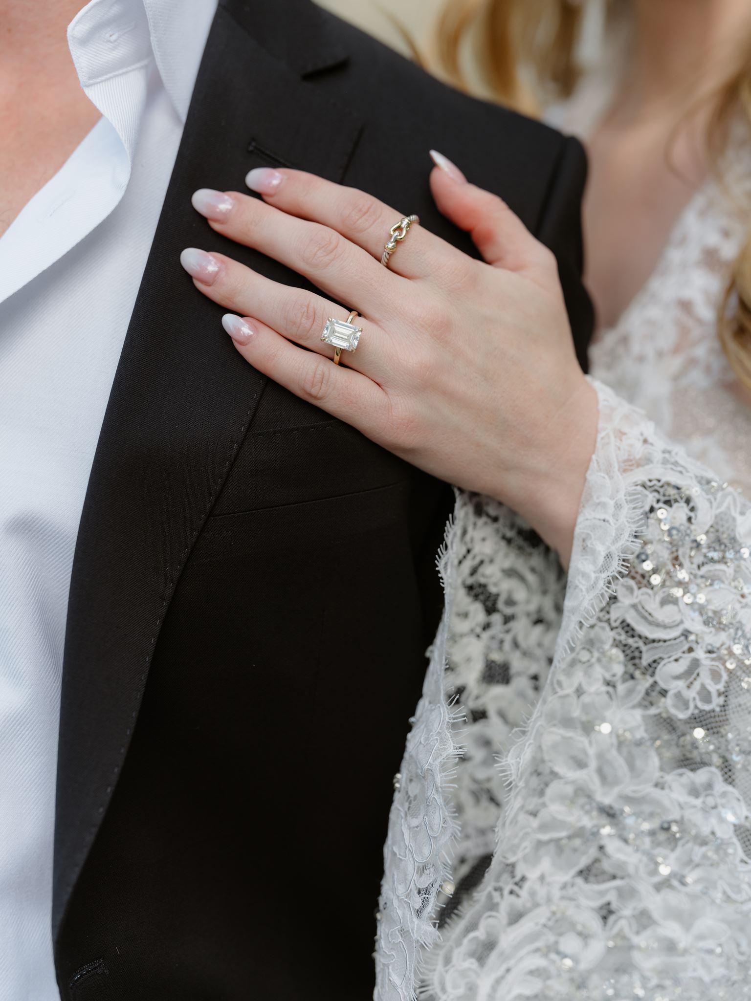 Erica’s wedding ring and lace sleeve resting against Evan’s dark suit.