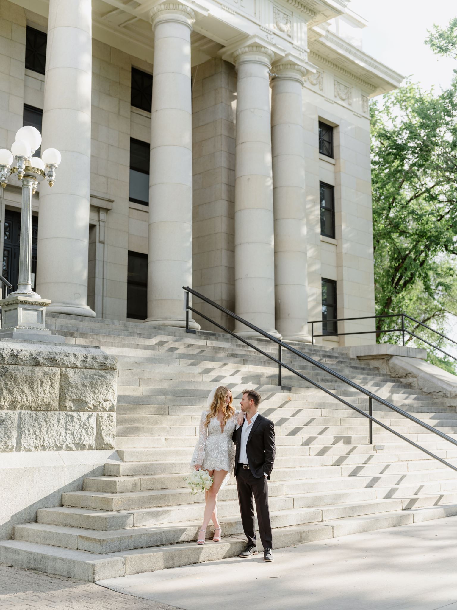The couple on a sunlit staircase beneath tall courthouse columns.