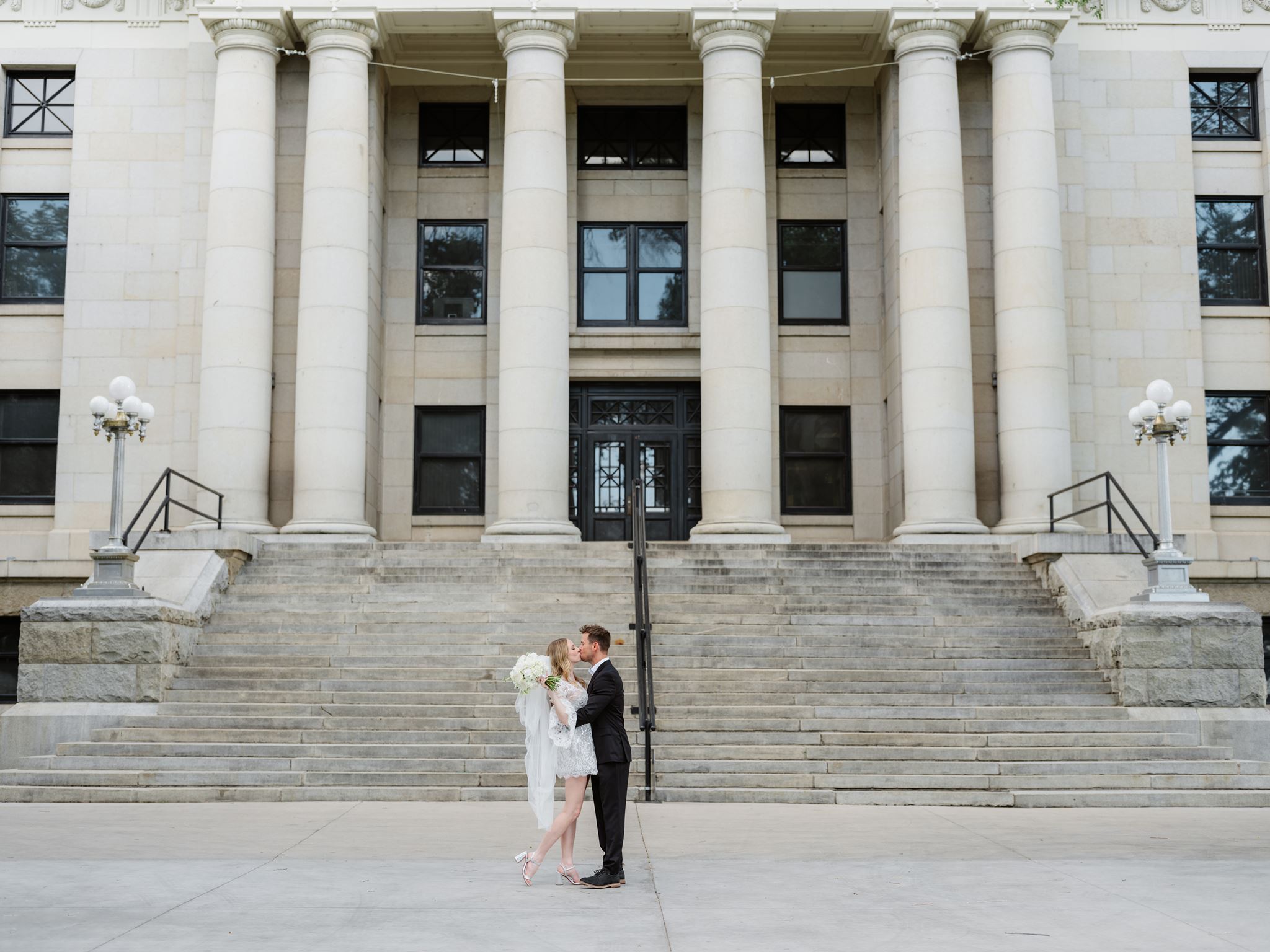 Erica and Evan kissing in front of the Yavapai County Courthouse columns.