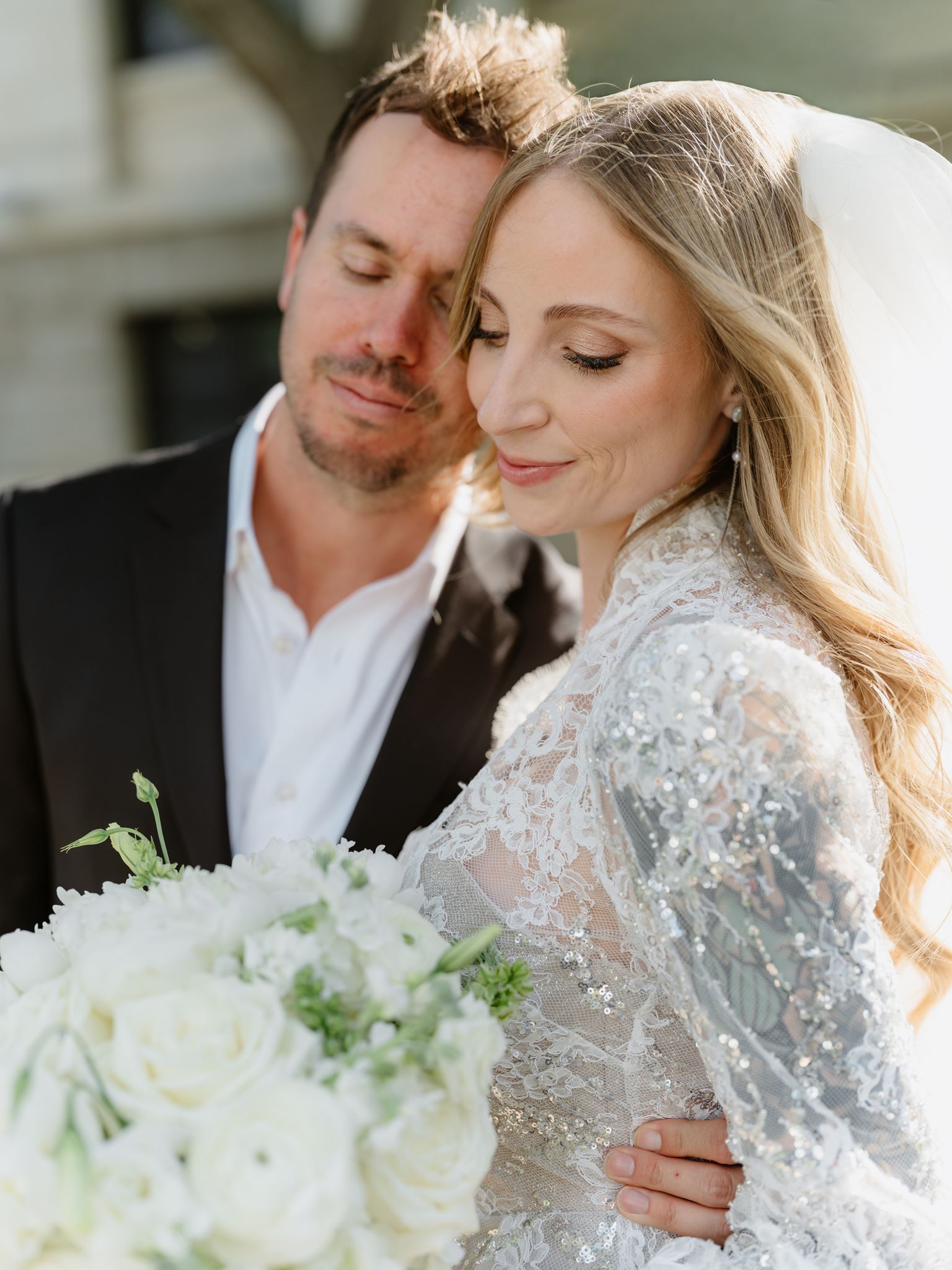 Close portrait of Erica leaning into Evan with her white bridal bouquet.