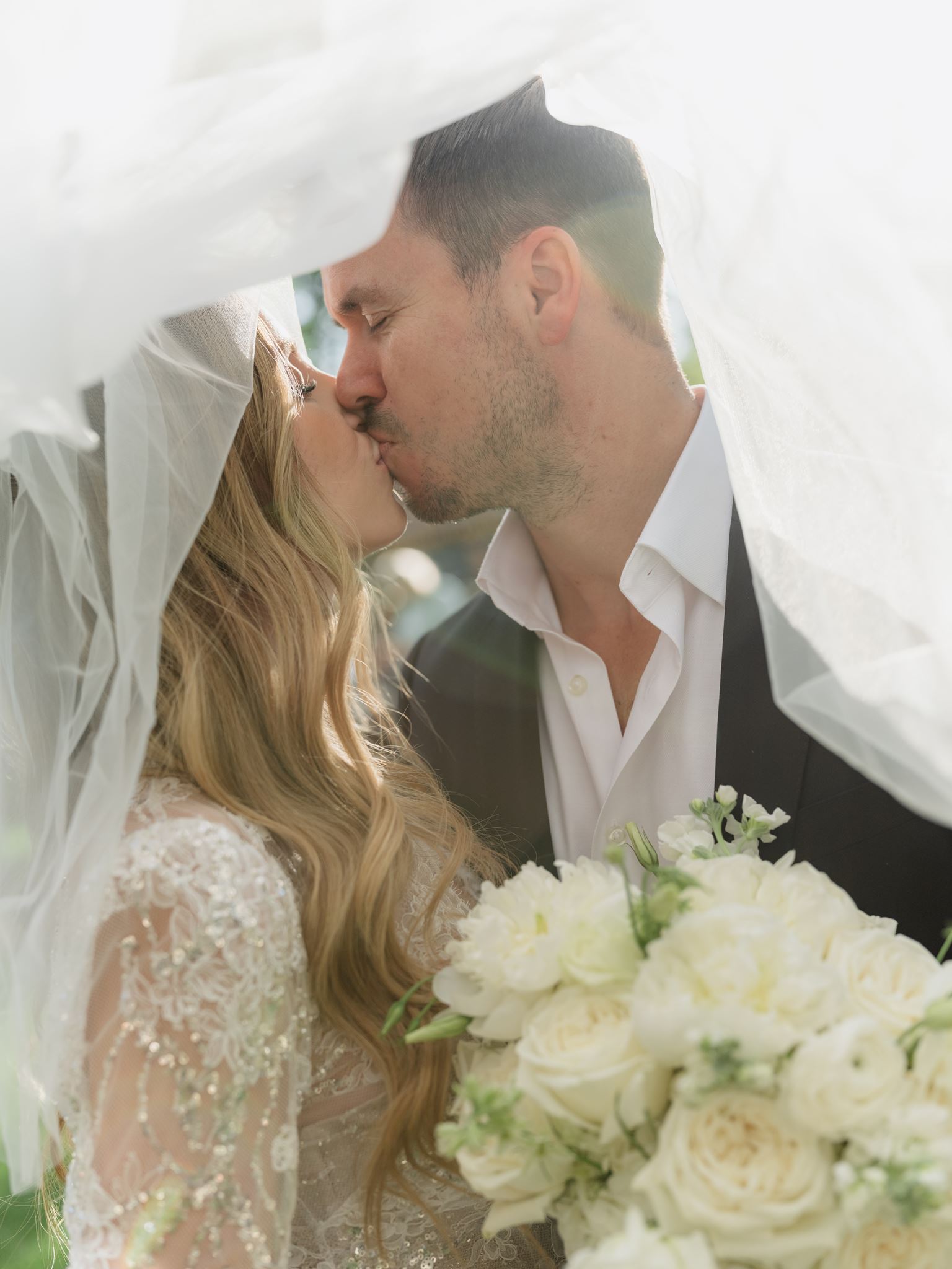 Erica and Evan kissing beneath her sheer bridal veil.