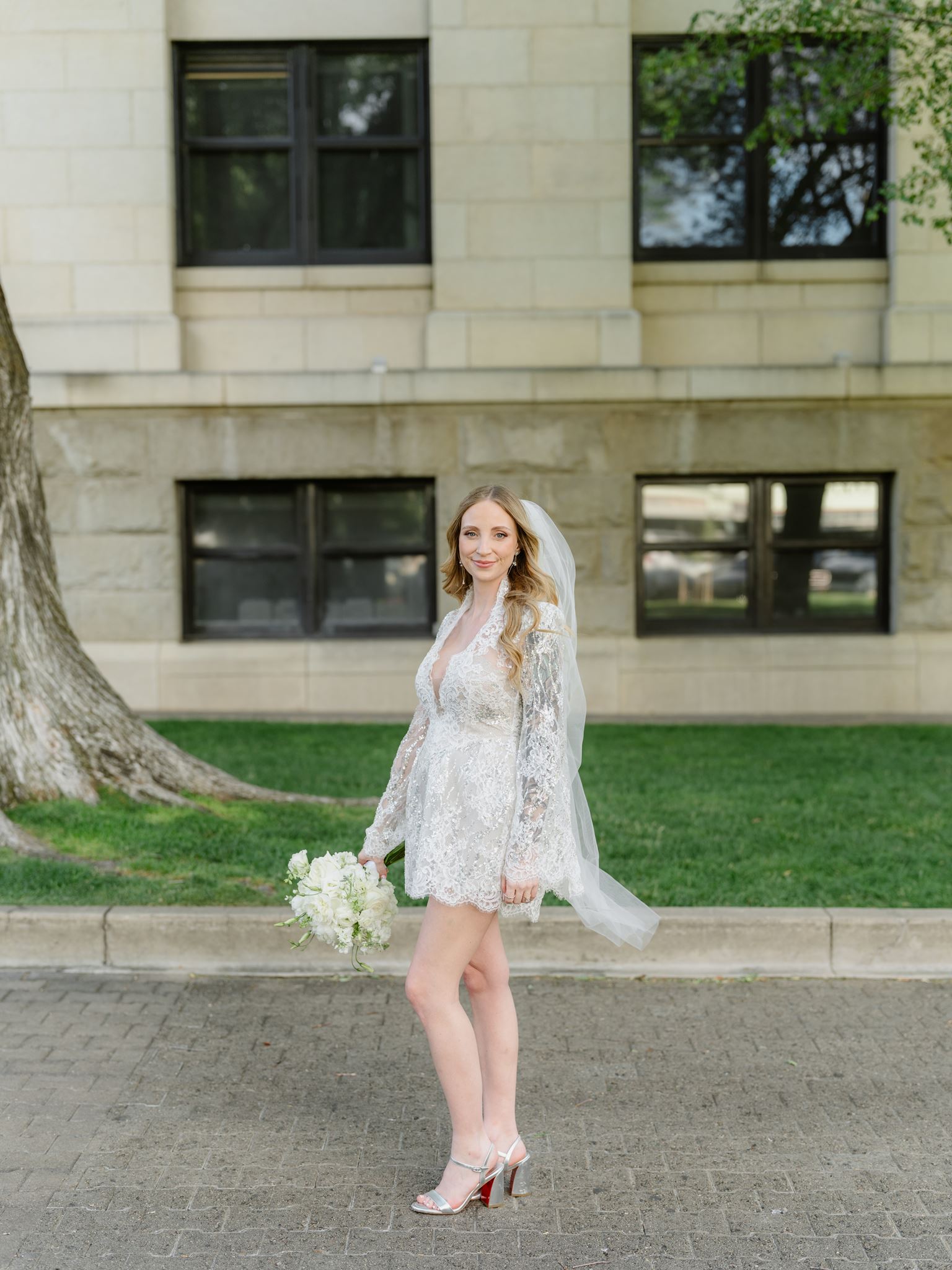 Erica in a short lace wedding dress and long veil beside the courthouse.