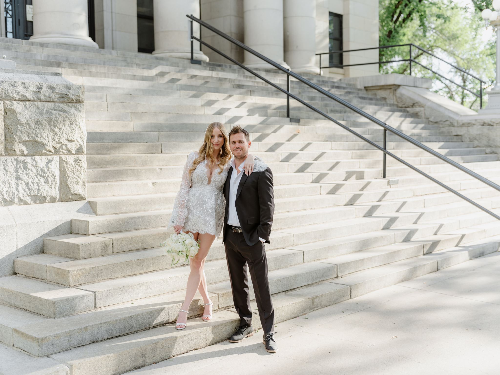 Erica and Evan standing together on the sunlit stone steps.