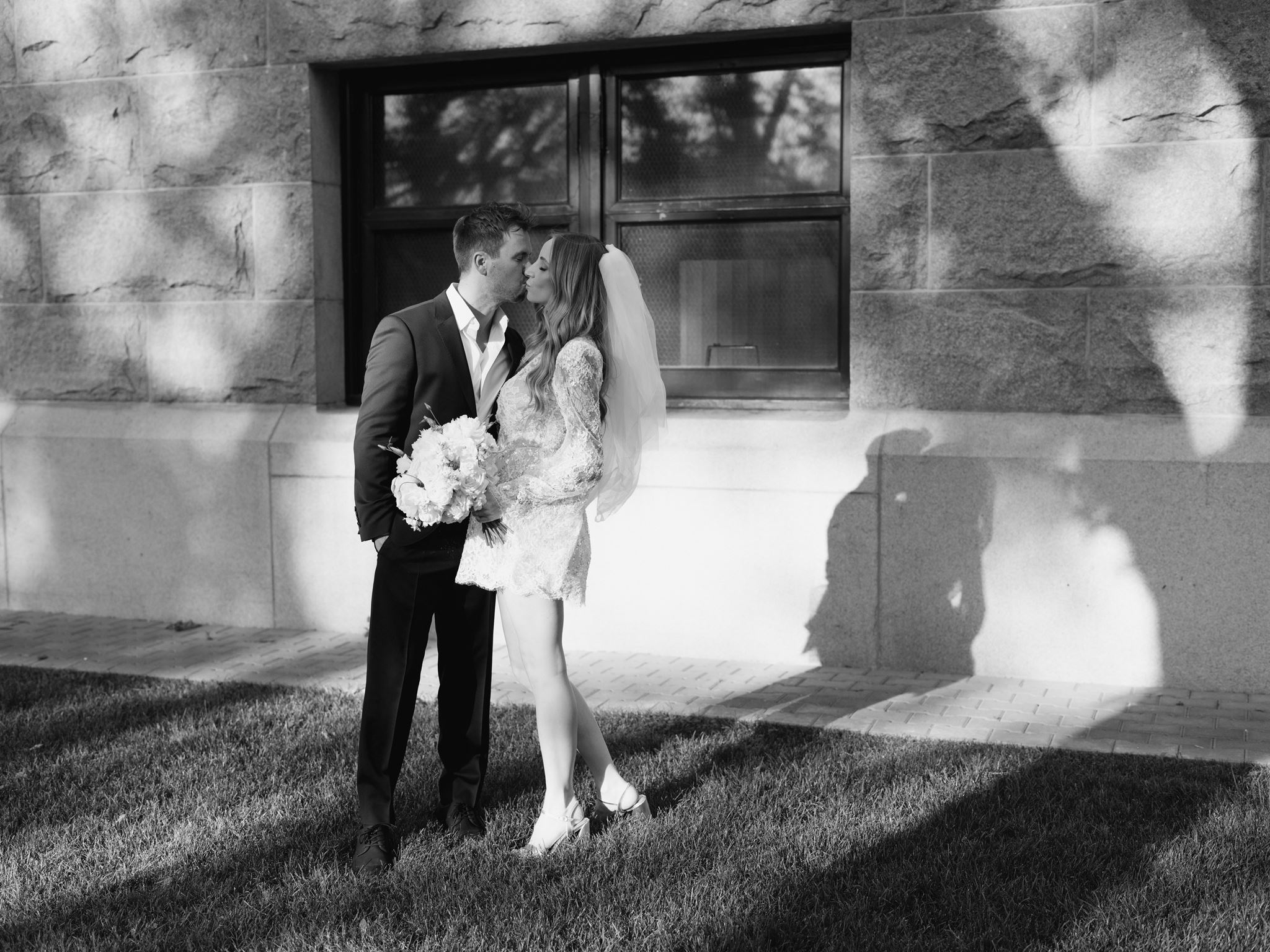 Black and white portrait of the couple beside a courthouse window with their shadows on the stone wall.