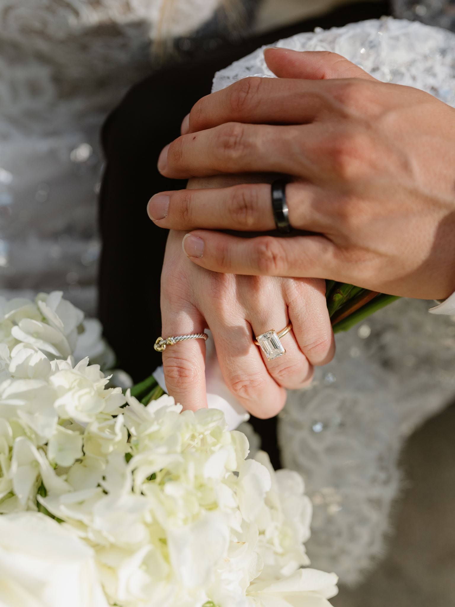 Close view of the couple’s wedding rings and hands above white flowers.
