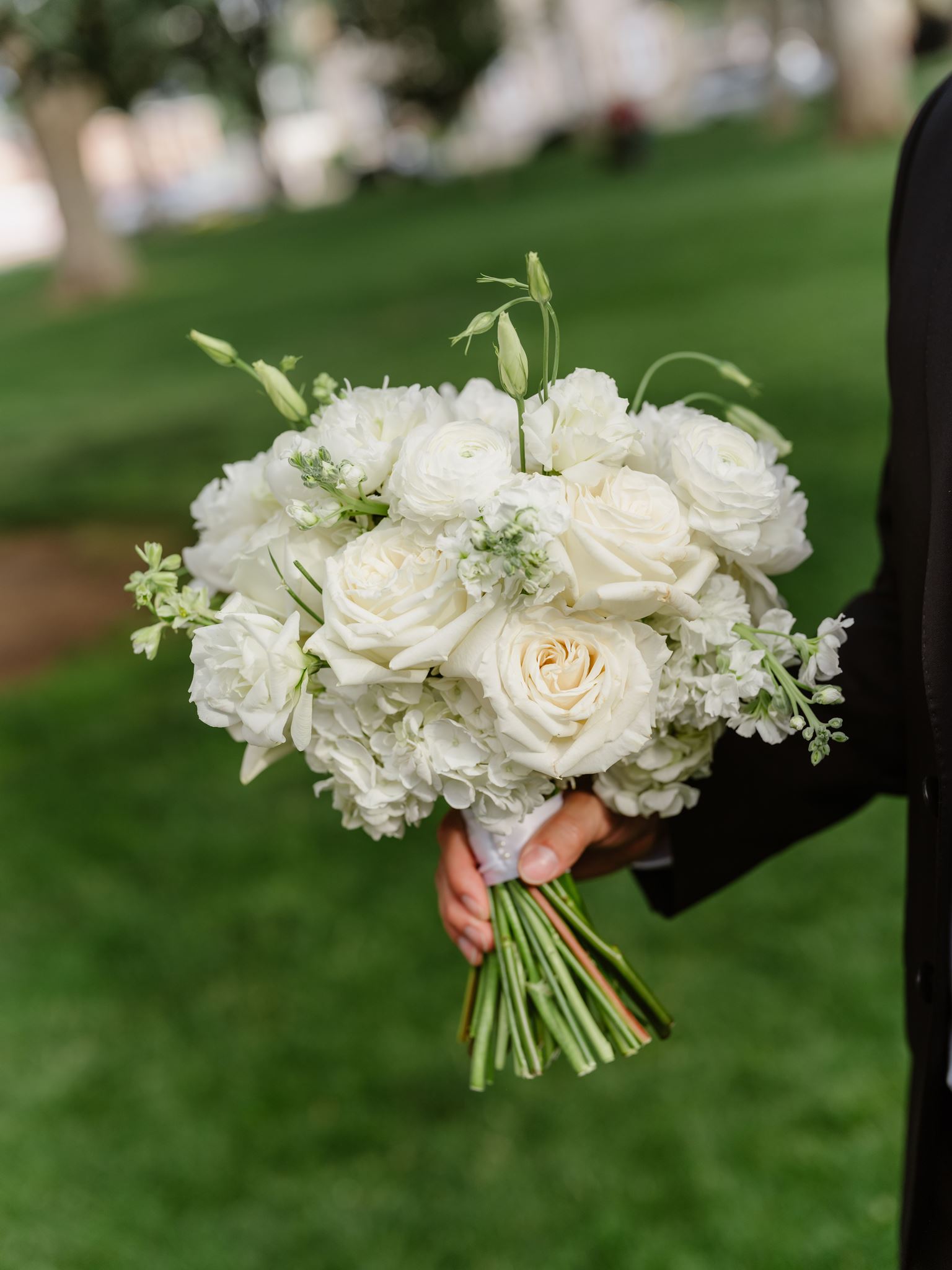 White bridal bouquet held above the green courthouse lawn.