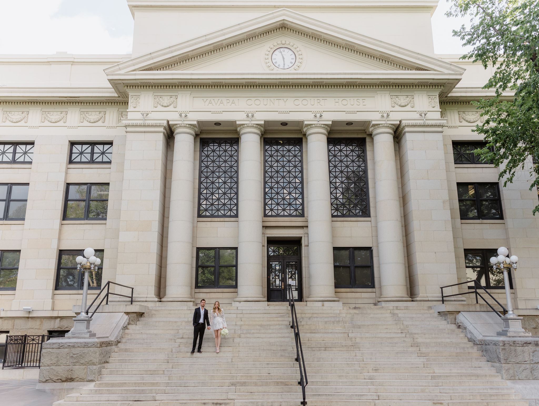 Wide view of Erica and Evan on the steps beneath the courthouse pediment and clock.