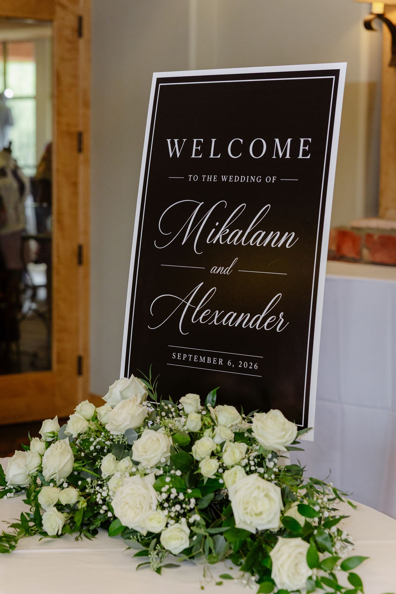 Mikalann and Alexander’s black wedding welcome sign surrounded by white flowers
