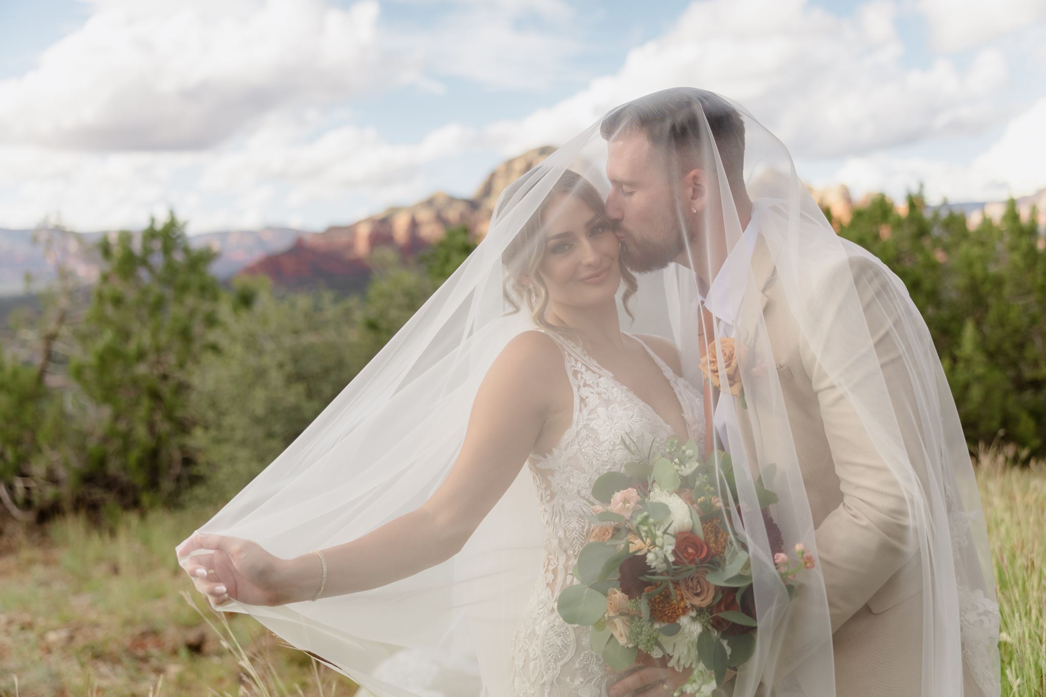 Kylie and Peyton sharing a kiss beneath her veil during their Sedona wedding portraits.