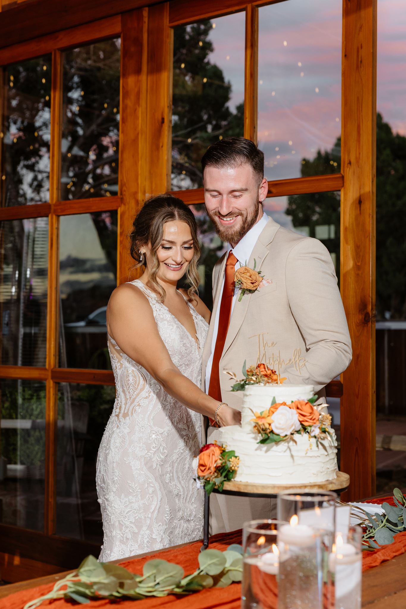 Kylie and Peyton smiling as they cut their flower-decorated wedding cake.